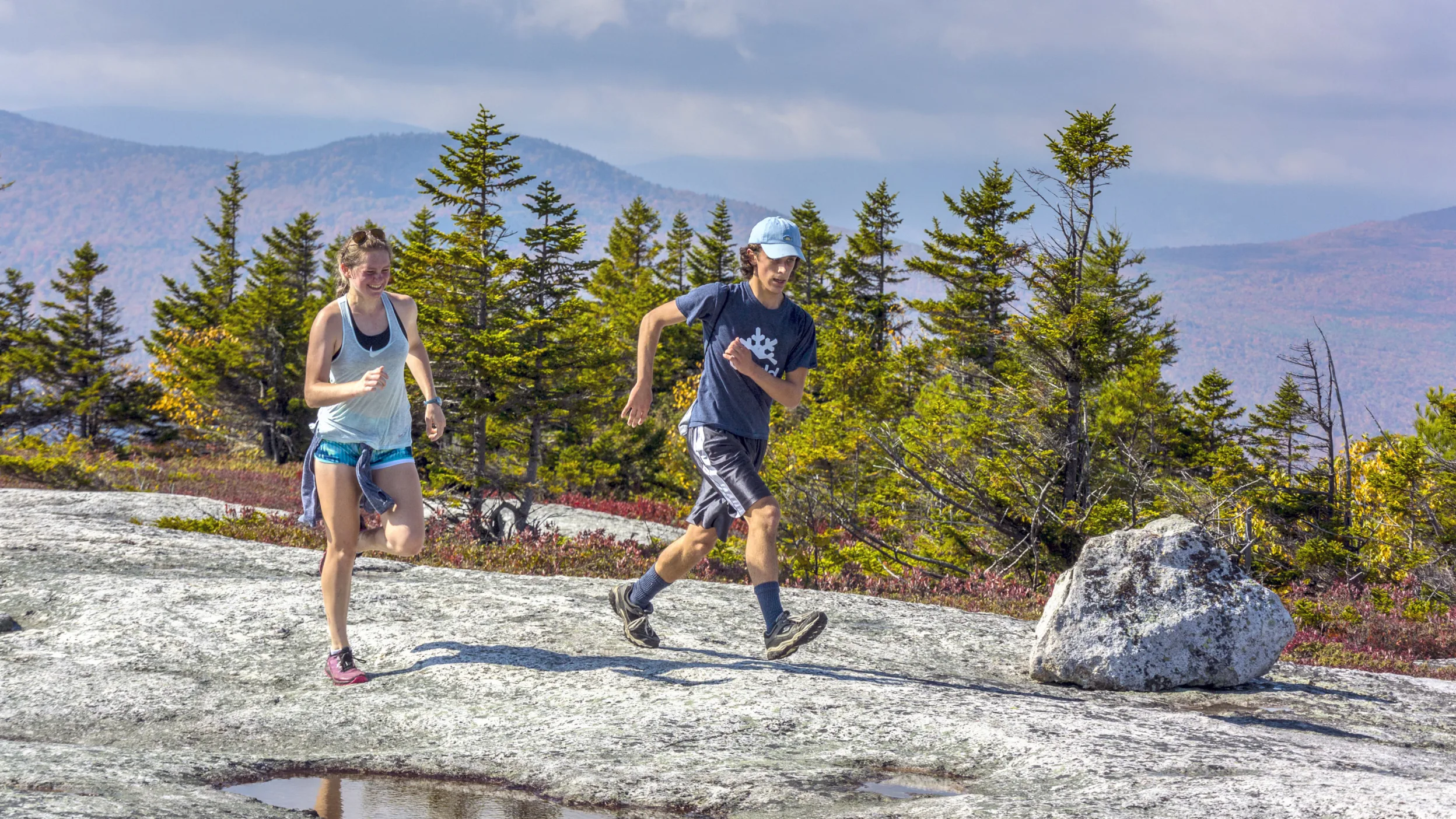 Two people running on a rocky terrain, surrounded by forest