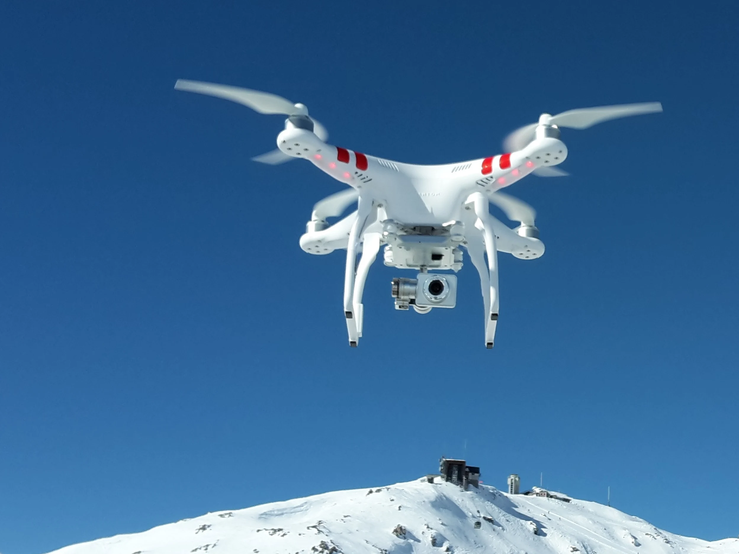 A white drone hovers over a snow covered mountain landscape