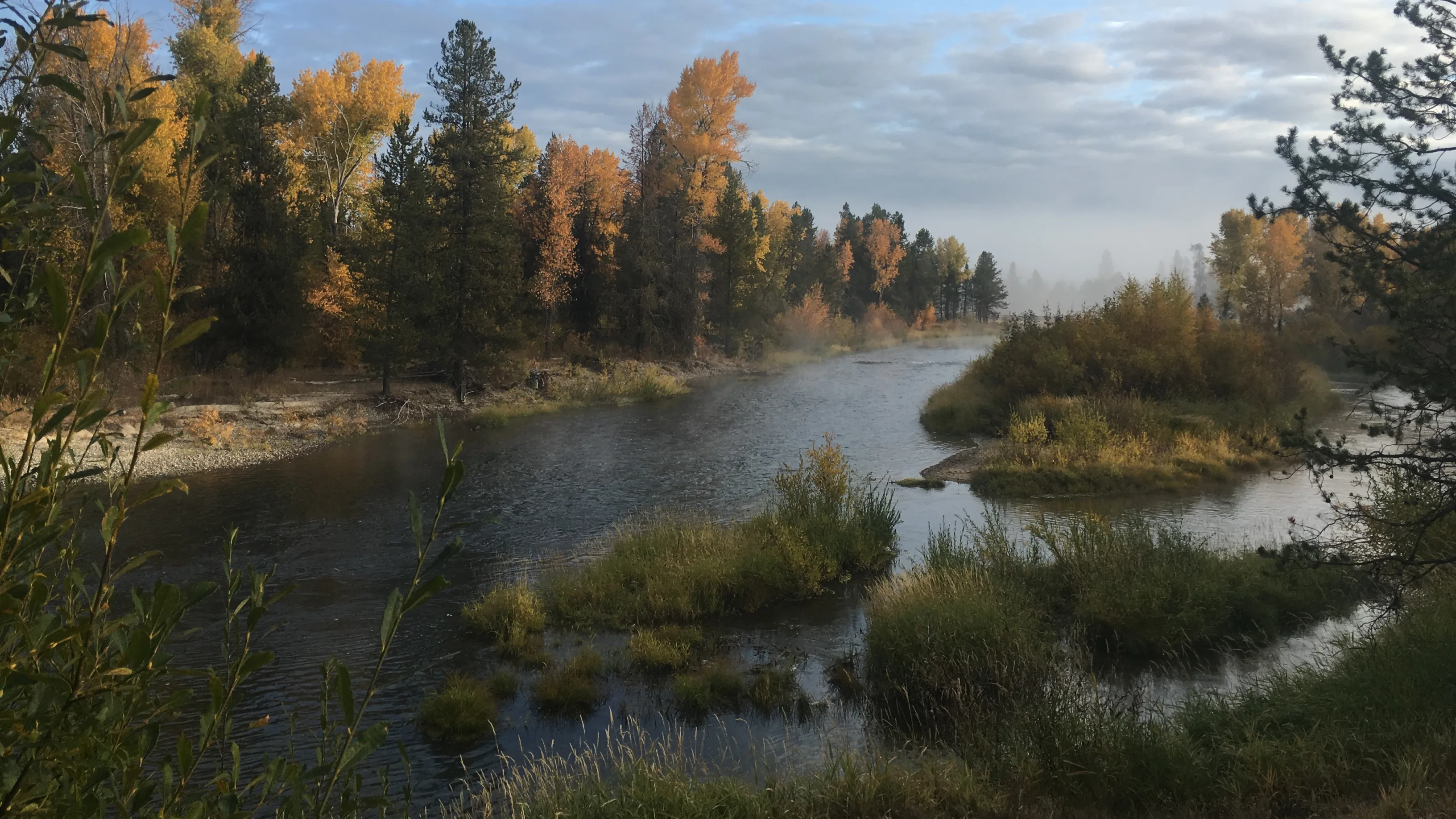 A river surrounded by orange, green and red trees, with a few tree and grass filled islands.
