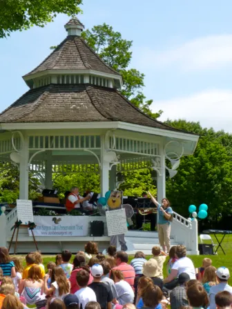 A gazebo with a band inside of it playing with children and families sitting around it.