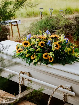 A casket made of wood with a bouquet of flowers on it, next to a pile of dirt with shovels in it