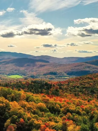 Overlooking a mountainous area with red, green and yellow trees in front of clouds