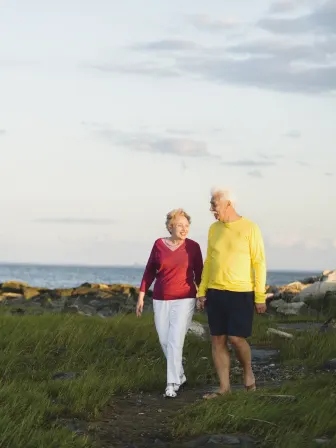 Two older people walking on a path with water behind them