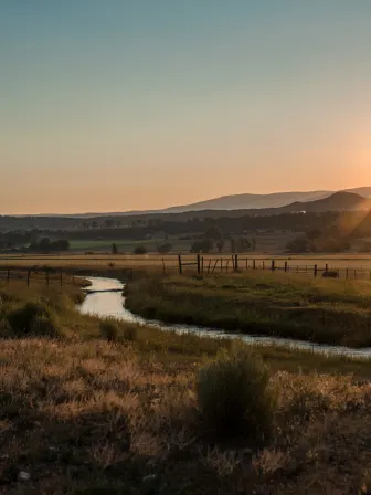 Sun setting over a field surrounded by mountains, with a stream going through the field