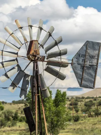 Photo of a windmill with mountains and trees behind it.