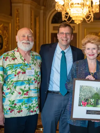 Three men and one woman present an award to a female senator, positioned in the center.