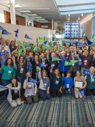 A large group of people in business casual clothing holding green and blue flags that say accredited or renewed.