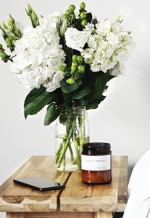 Fresh flowers in a vase and candles sitting on top of a side table