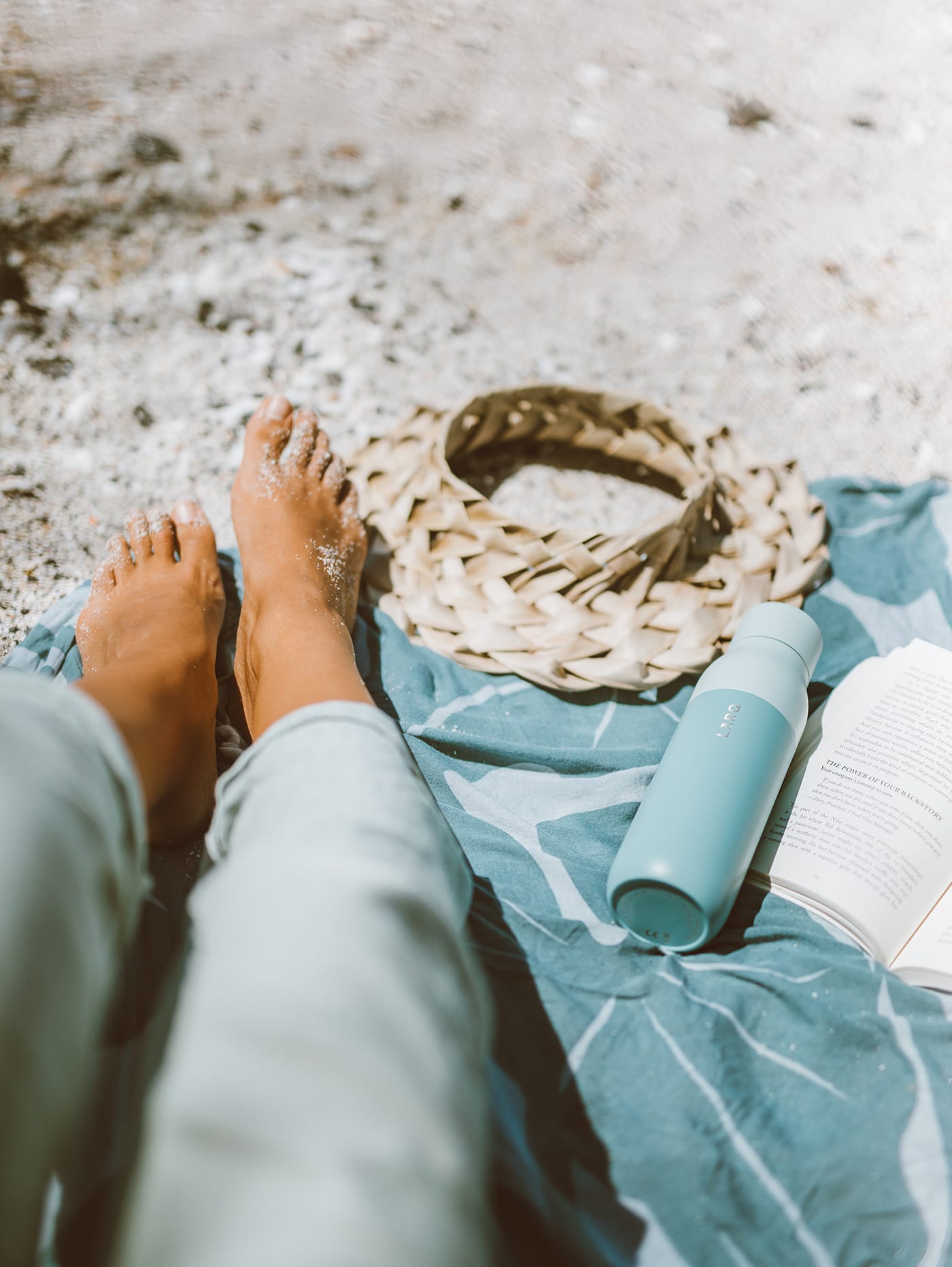 Elana Jadallah sits on blue beach towel with her seaside mint LARQ Bottle