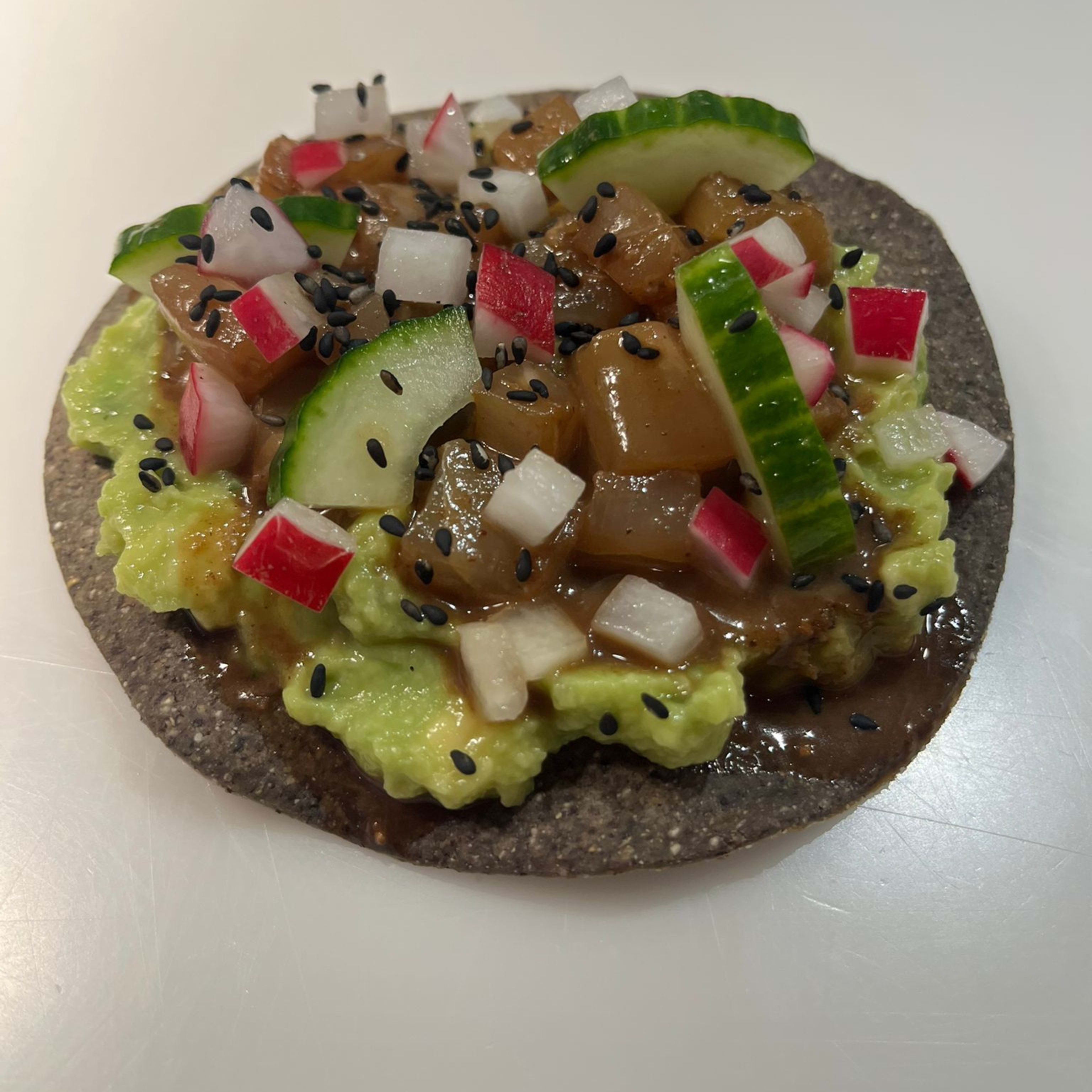 Tostada de ceviche de lubina, aguacate, jengibre, cilantro, pepino, sésamo negro y salsa macha