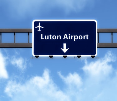 Wide view of Luton Airport sign with arrows pointing towards various terminals
