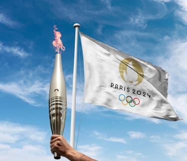 Hand holding the olimpic torch and a Olympic flag in the background