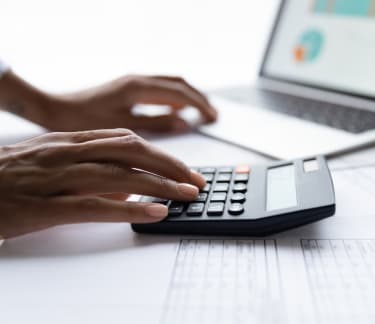 Individual multitasking with a calculator and laptop at a desk covered in financial documents