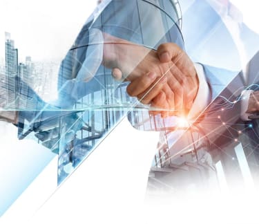 Two people shaking hands, with two people holding laptops in the background