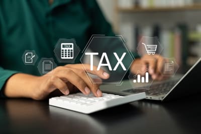 Person using a calculator and tying a laptop with the word Tax on the image