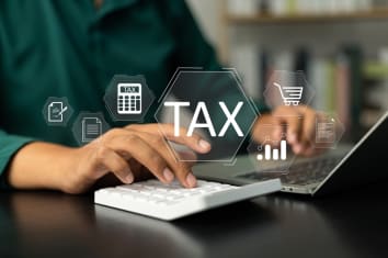 Person using a calculator and tying a laptop with the word Tax on the image