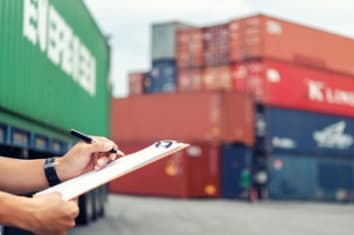 Person writing a document and shipping containers in the background