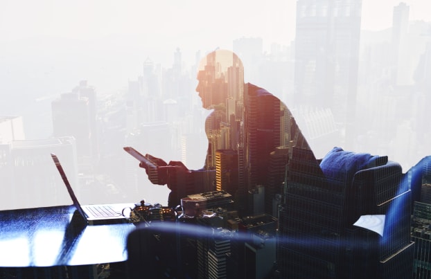 Man working with a laptop and holding a phone