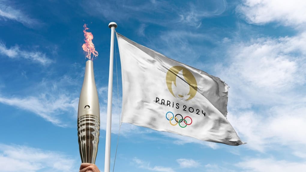 Hand holding the olimpic torch and a Olympic flag in the background