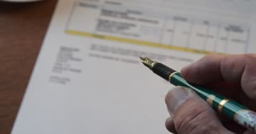 Person holding a pen and a document is in the background