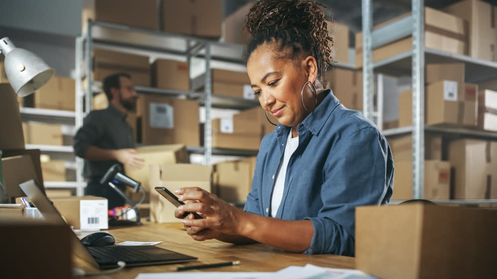 Woman business owners surrounded by boxes looking at a mobile