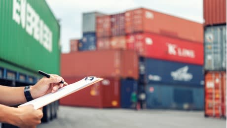 Person writing a document and shipping containers in the background