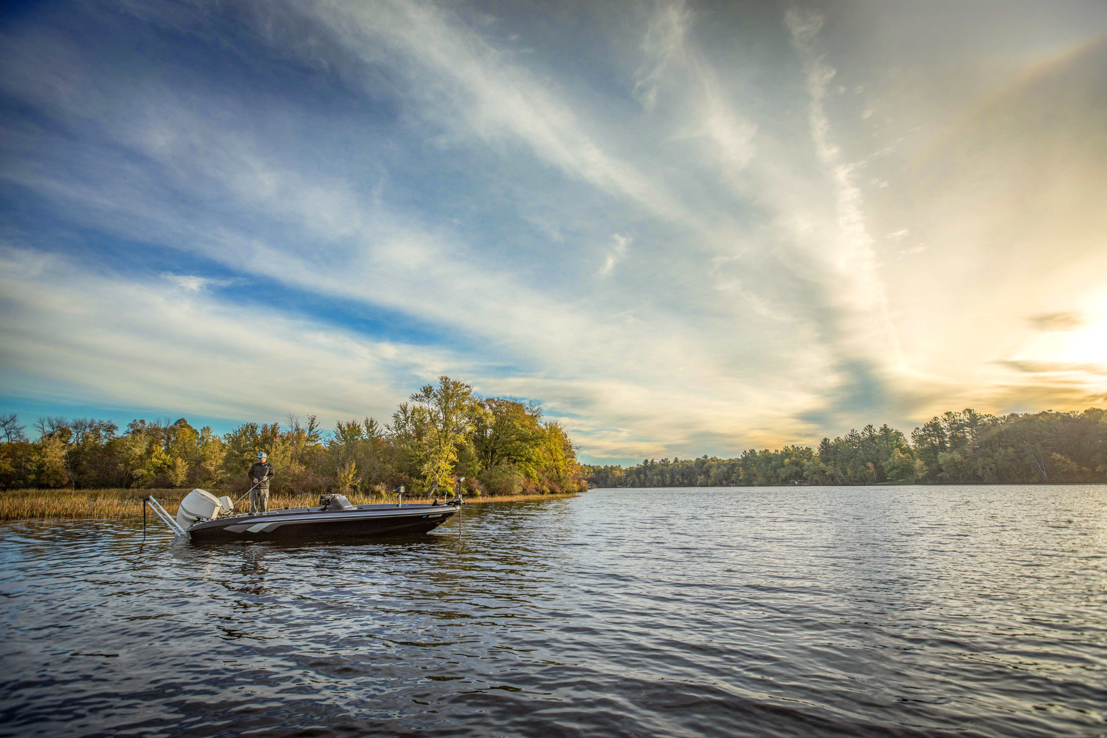Weekend angler fishing from a bass boat anchored in a freshwater cove at golden hour, Lewmar Axis 6 electric anchor on transom