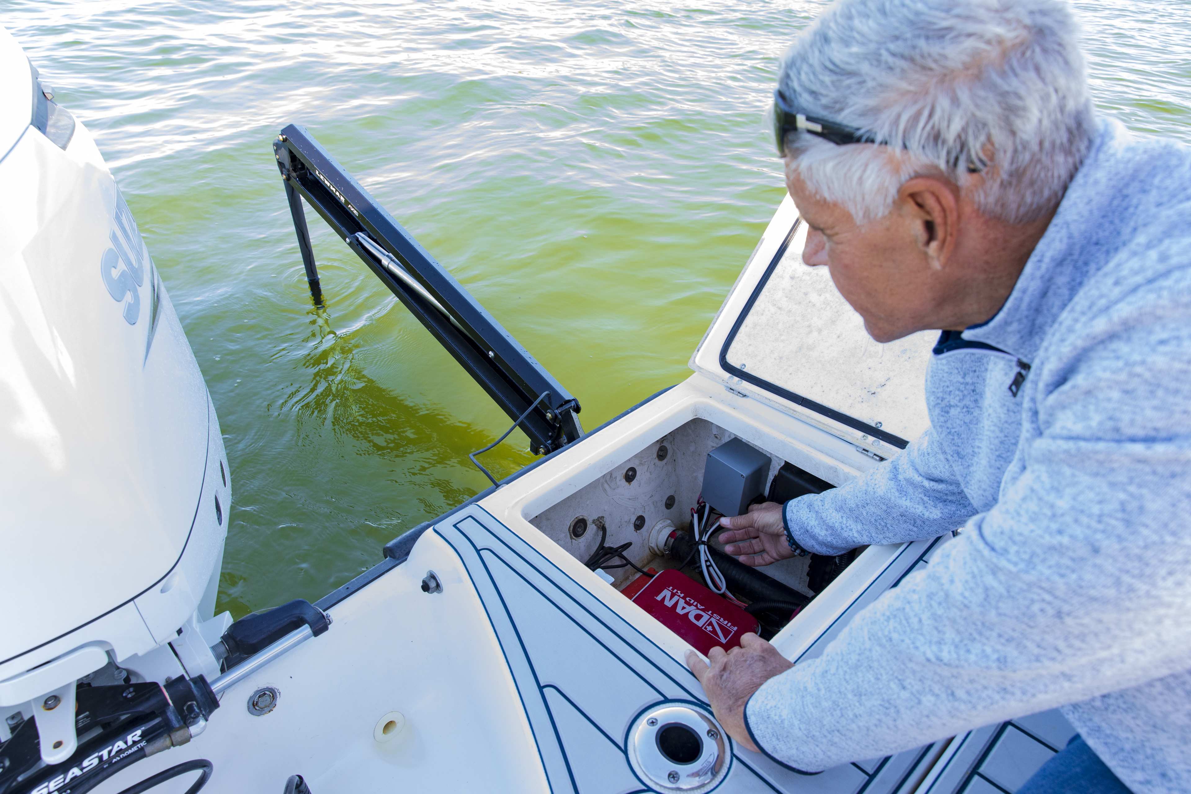 Lewmar shallow water anchor deployed beside a white outboard while a person works in the open battery compartment