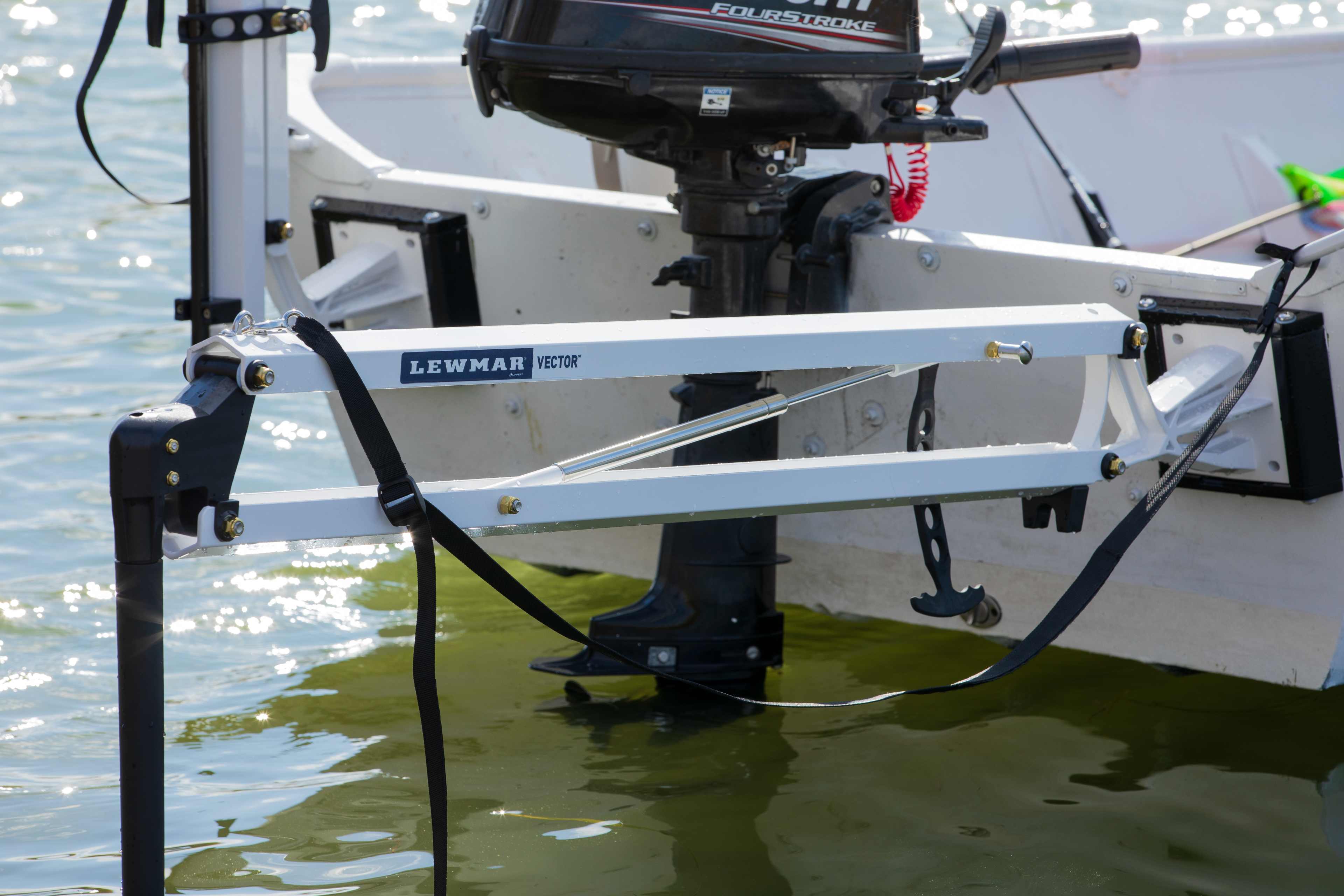 Close-up of a white Lewmar Vector shallow water anchor and its black tensioning strap, mounted beside an outboard