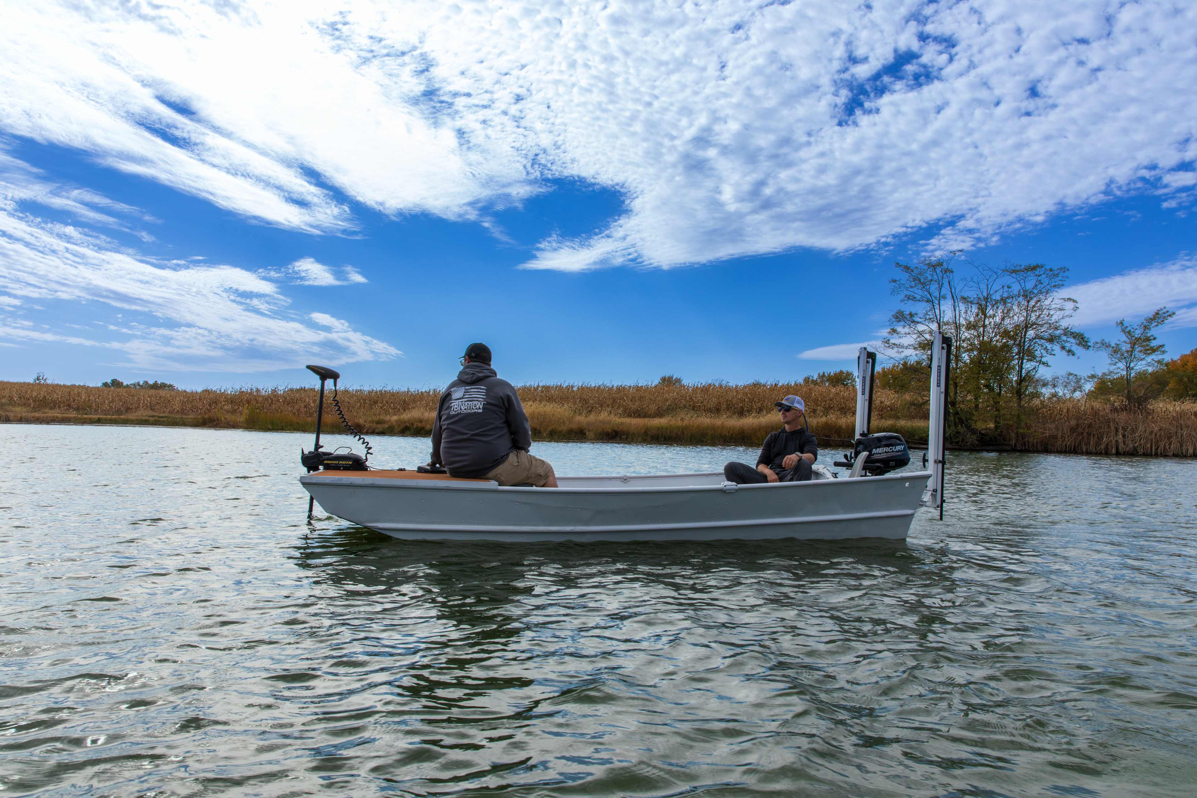 Two anglers in a jon boat with a trolling motor at the bow and a shallow water anchor stowed at the transom