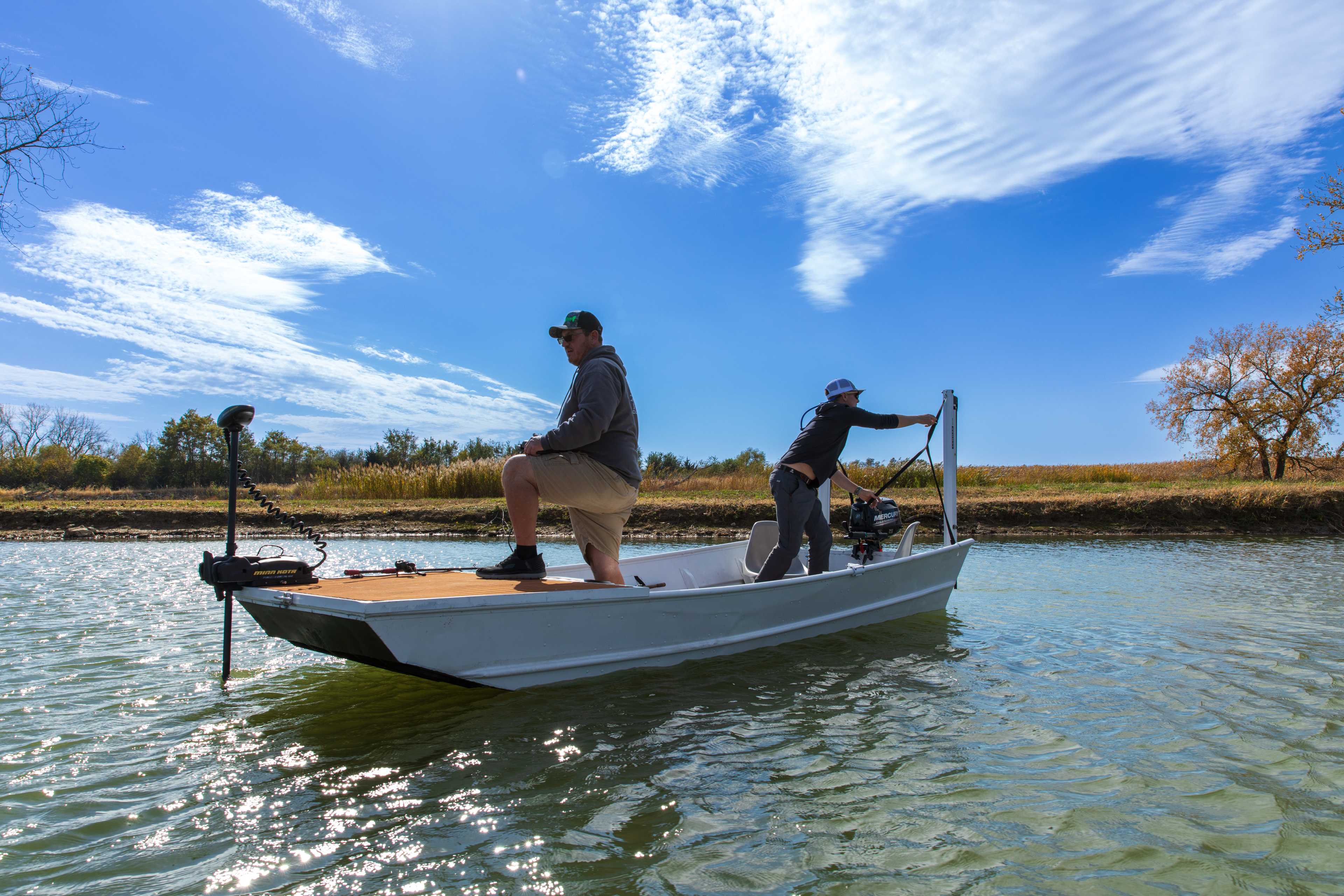 One angler fishing from the bow while another deploys a shallow water anchor at the stern of a jon boat
