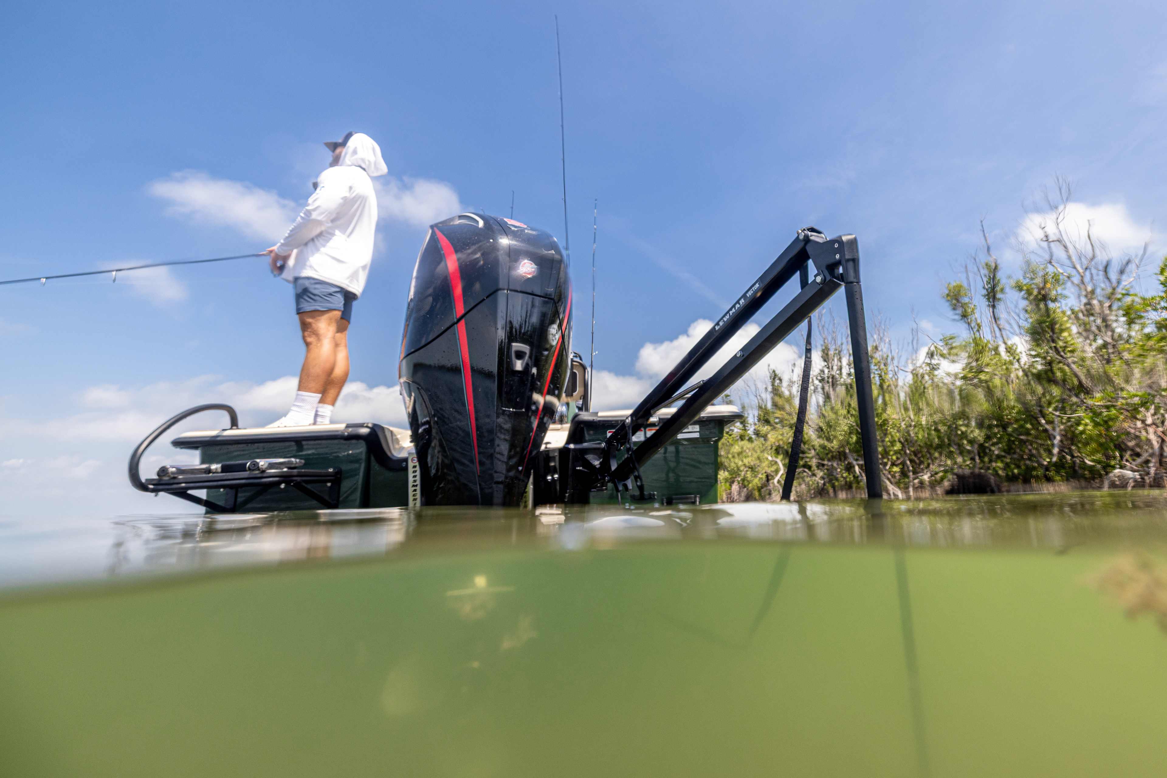 Angler fishing from the bow of a skiff while a Lewmar shallow water anchor holds the boat along a mangrove shoreline