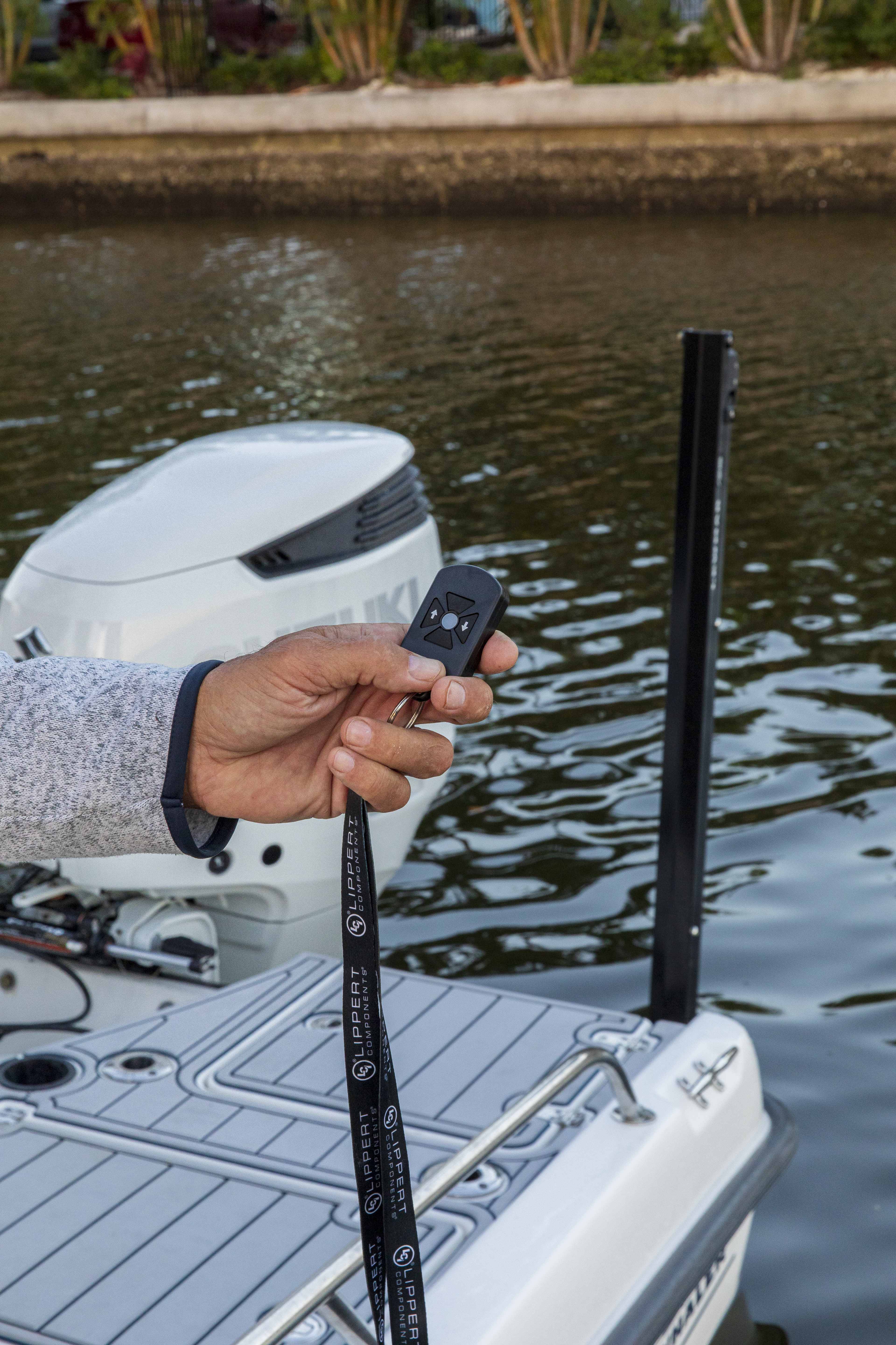 Hand holding a Lewmar keychain remote beside a deployed shallow water anchor and an outboard