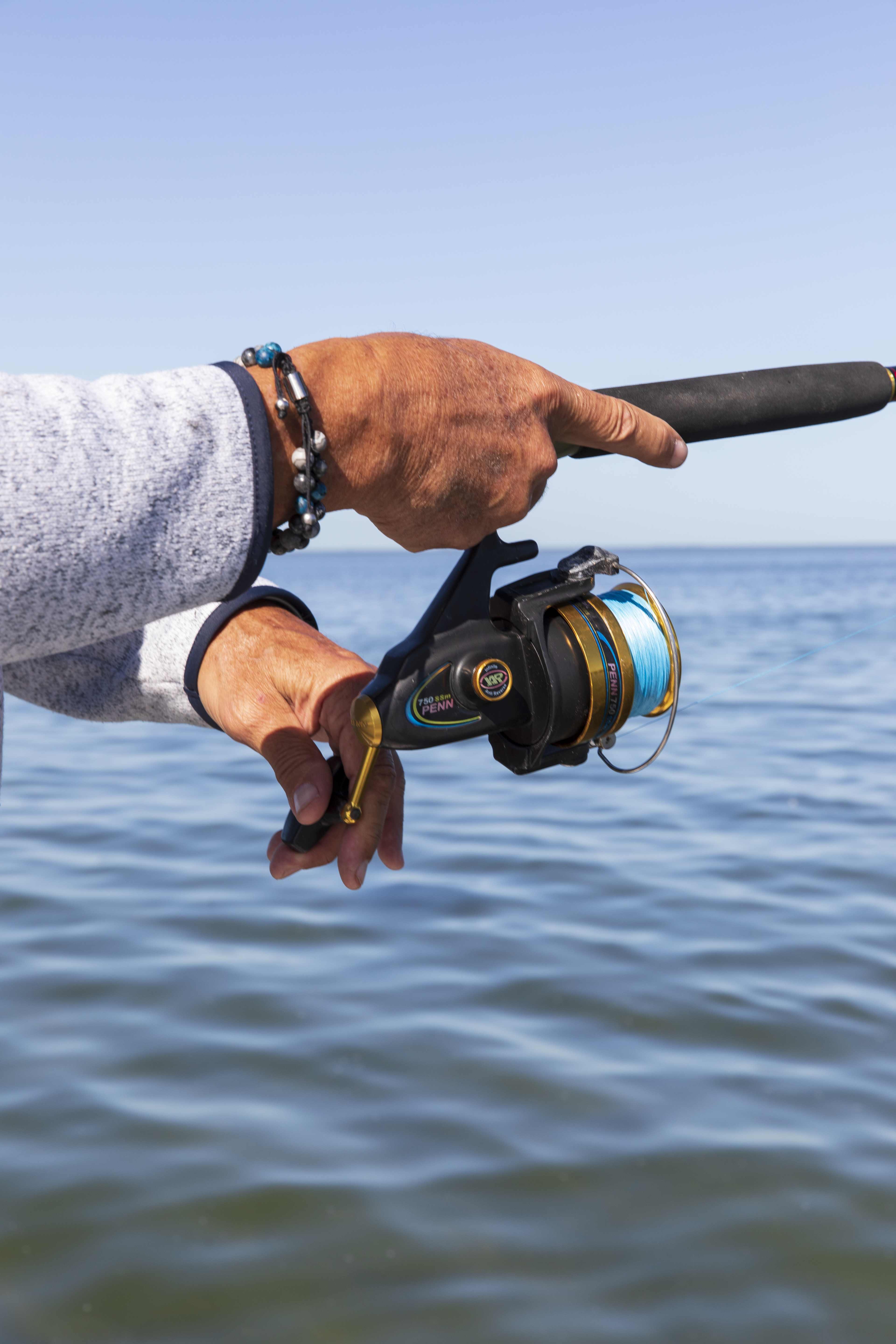 Close-up of an angler's hands working a spinning reel over open water