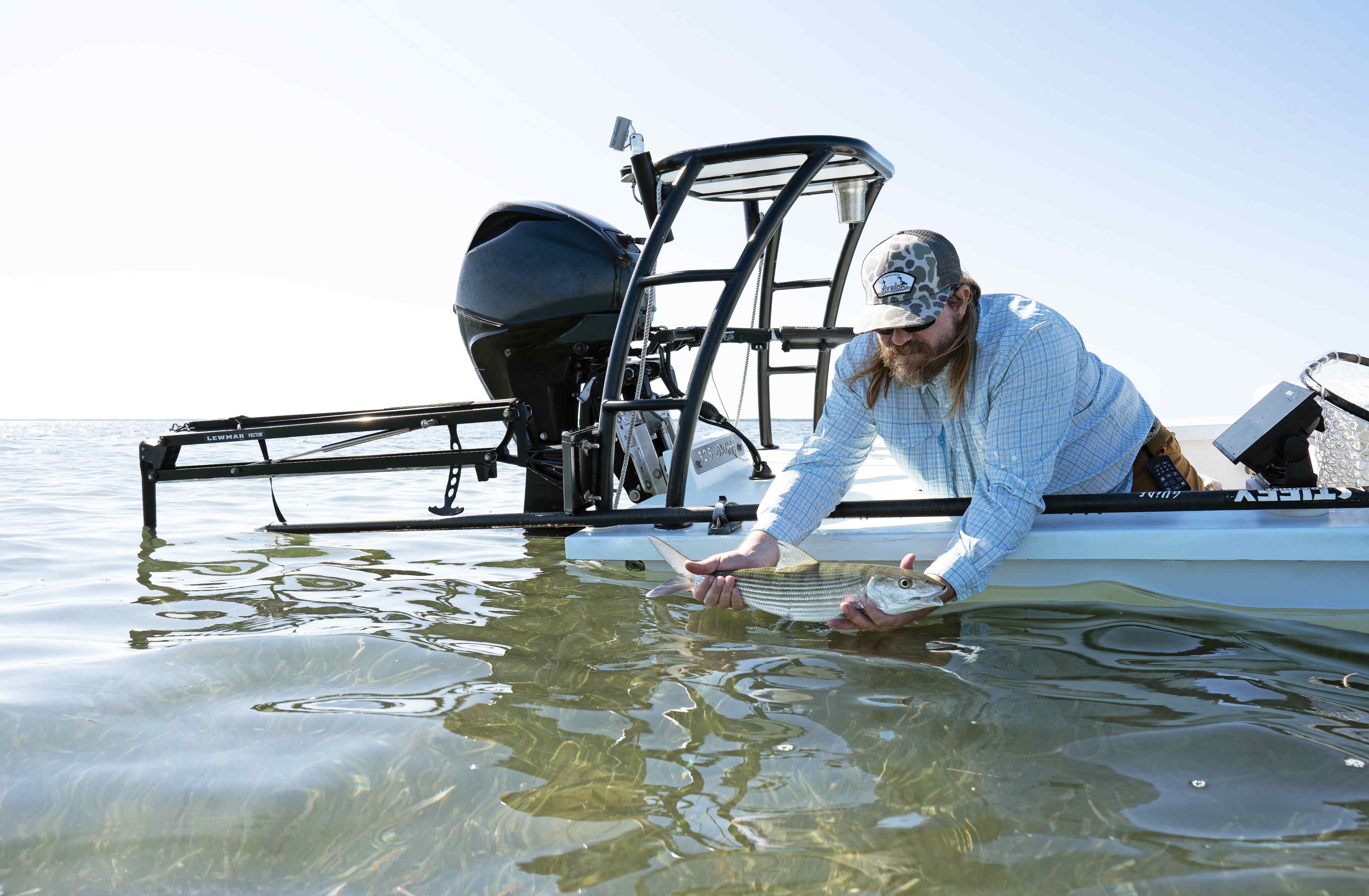 Angler releasing a fish from a skiff while a white Lewmar Vector shallow water anchor holds the boat