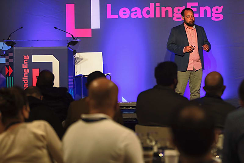 A speaker on stage at LeadingEng London 2022, watched by audience members seated at tables