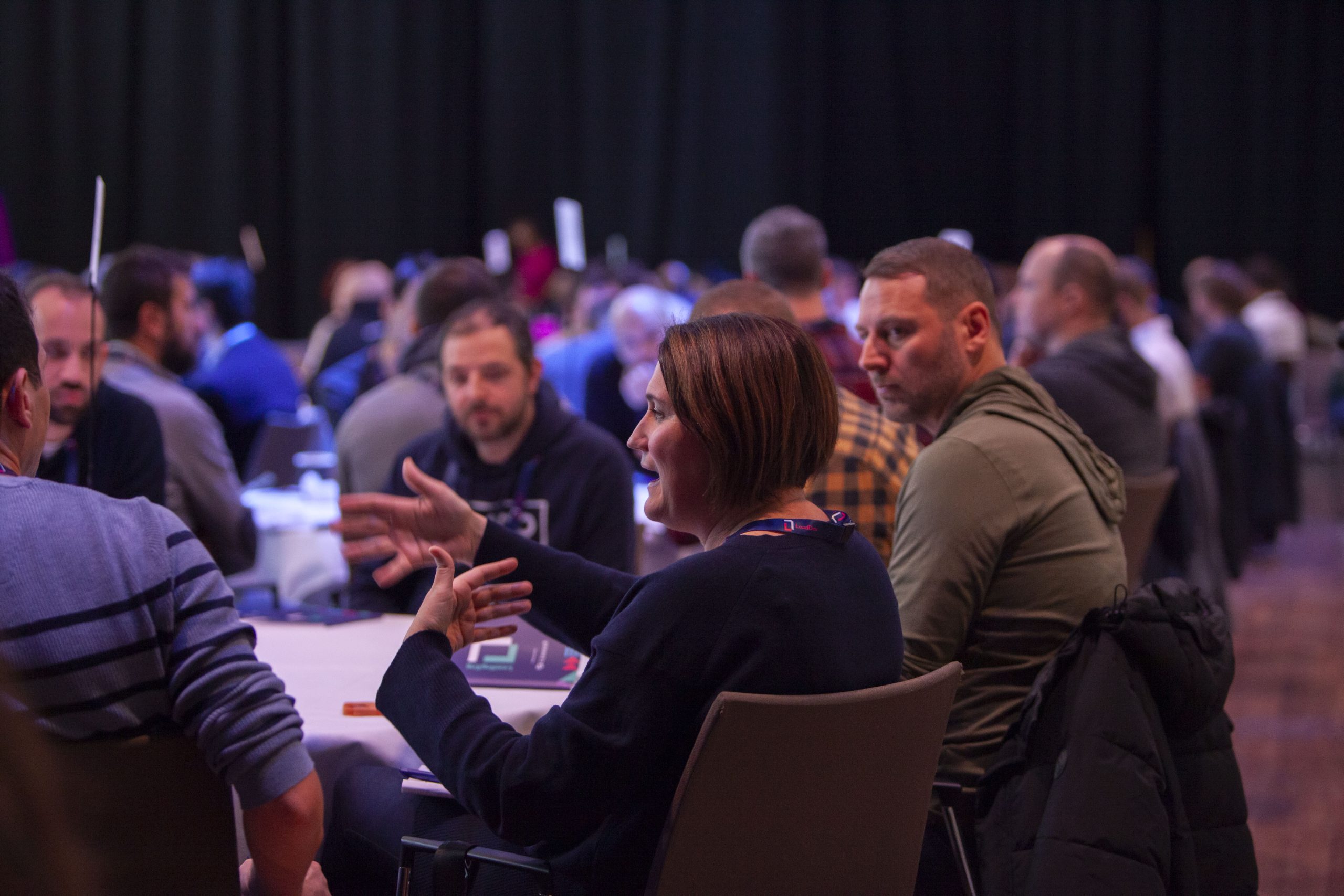 Participants at a workshop talk around a roundtable with other tables in the background