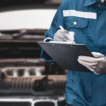 Mechanic inspecting car engine with clipboard