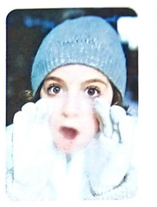 A person wearing a light blue knit hat and white mittens holds fluffy white material, possibly snow, around their face. Their eyes are wide and their mouth is open in surprise.