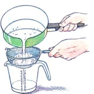 A hand pours liquid from a saucepan through a sieve into a measuring cup.