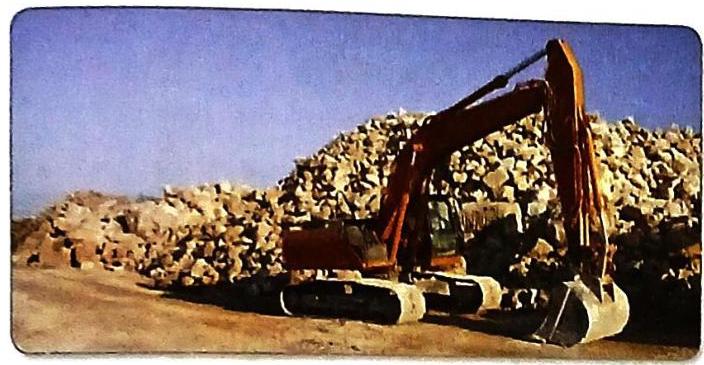 An orange excavator operates near a large pile of light-colored rocks under a clear blue sky.