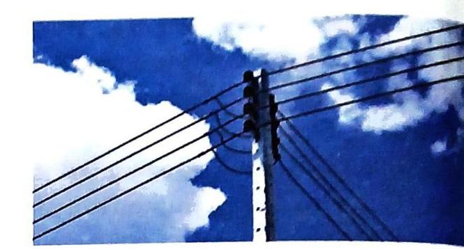 A utility pole with multiple wires stretches across a blue sky filled with white clouds.