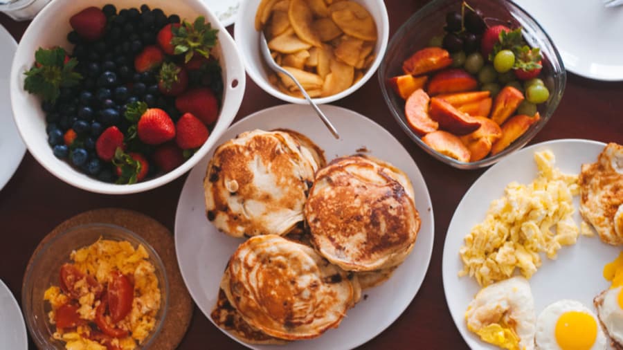 Different foods like eggs, muffins, strawberries, blackberries, tomatoes in separate plates on a white table