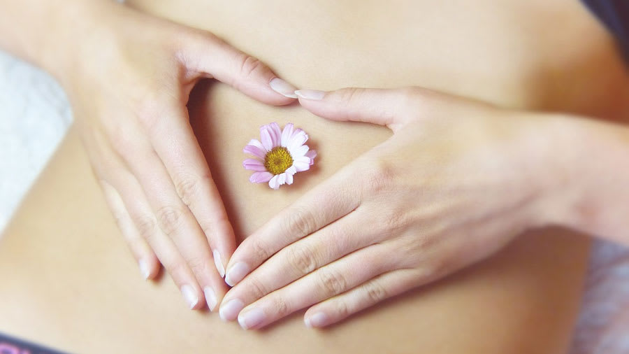 Woman with flower on bare belly and heart shape of hands representing integrative dermatology