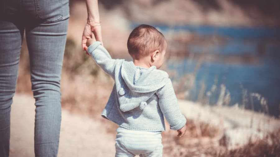 Child with blue hoodie walking on beach while holding an adult's hand