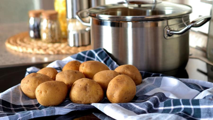 Potatoes boiled and cooled on a towel on a table in kitchen next to boiling pot