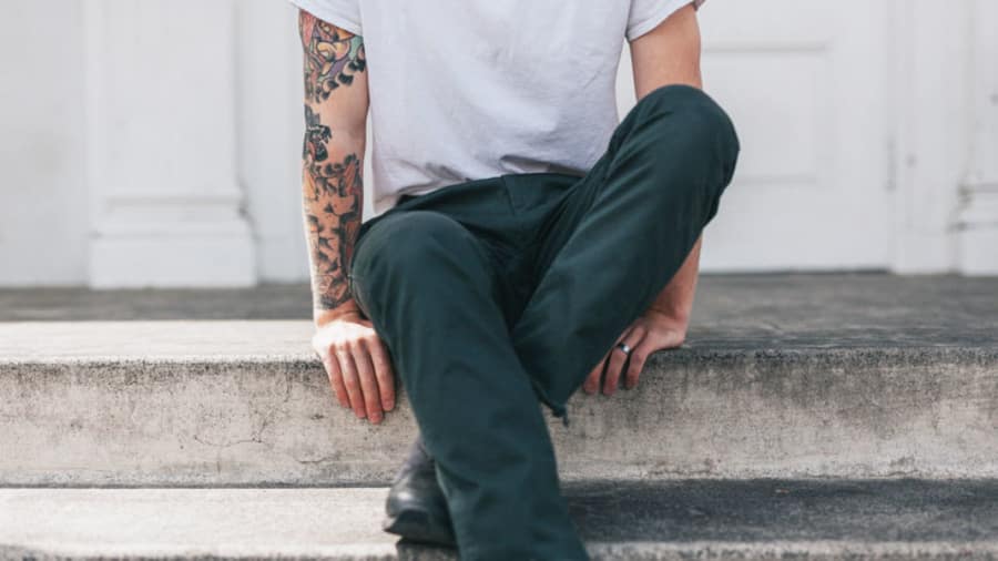 Man sitting cross-legged on steps with jeans, white tee shirt, and tattoos on right arm