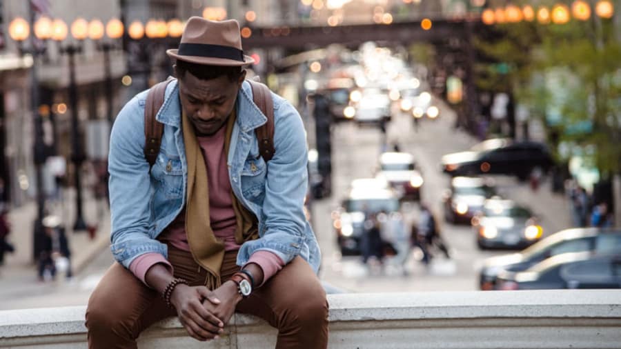 Man with hat sitting on overpass with head down and looking depressed