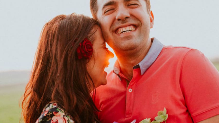 Man in red shirt laughing with woman who is hugging him with sunset in background