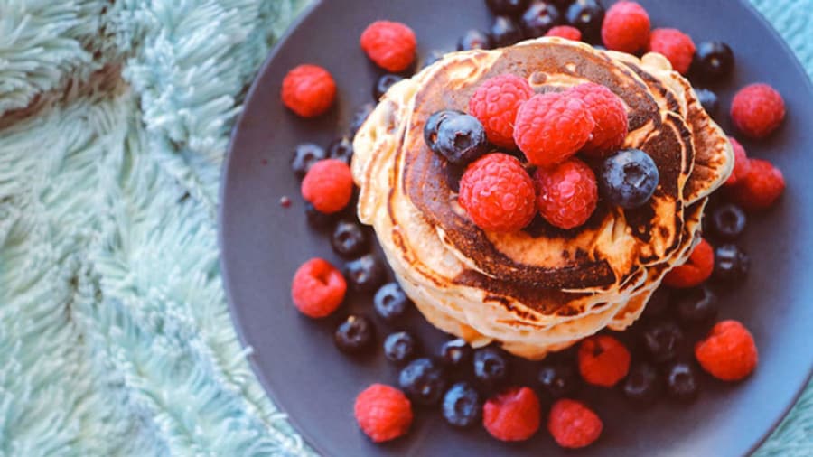 stack of pancakes with raspberries and blueberries on blue plate on blue carpet